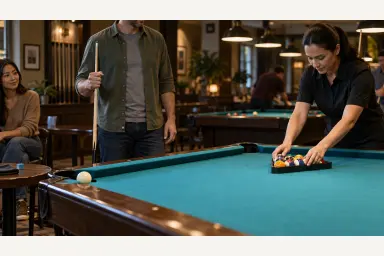 Pool players checking a clear table area while an attendant sets a rack and cues are held safely away from the cloth